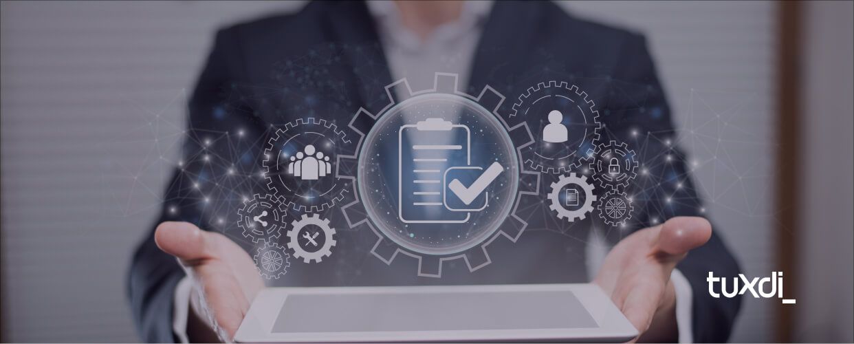 Persona sosteniendo una tablet con iconos digitales de engranajes y procesos automáticos, representando la automatización de procesos empresariales. Logo de Tuxdi.